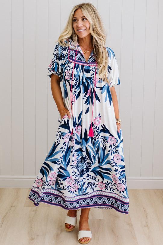 Blonde woman wearing a long printed maxi dress in blue and white with hot pink accents.
