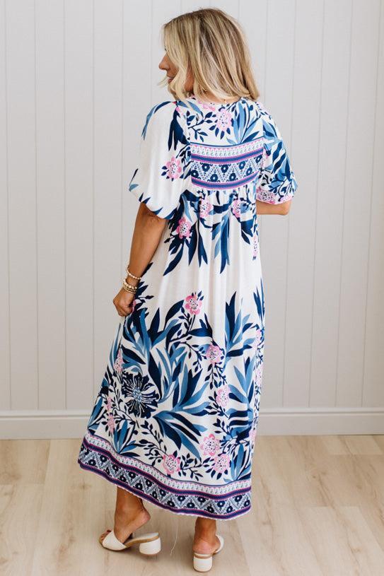 Blonde woman wearing a long printed maxi dress in blue and white with hot pink accents.