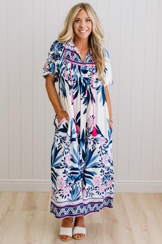 Woman wearing a floral dress standing against a white paneled wall.