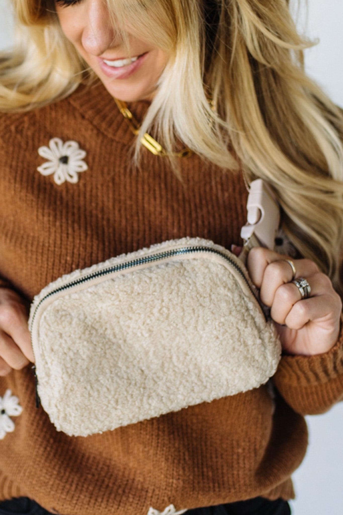 Person wearing a brown sweater with floral designs, holding a beige textured pouch.