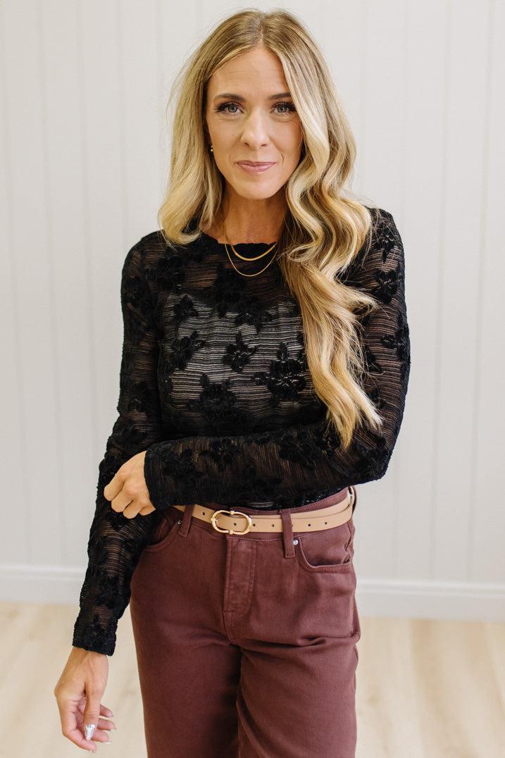 Blonde Woman Wearing A Floral Embroidered Stretch Lace Long Sleeve Top with Dark Jeans and Light Brown Belt.