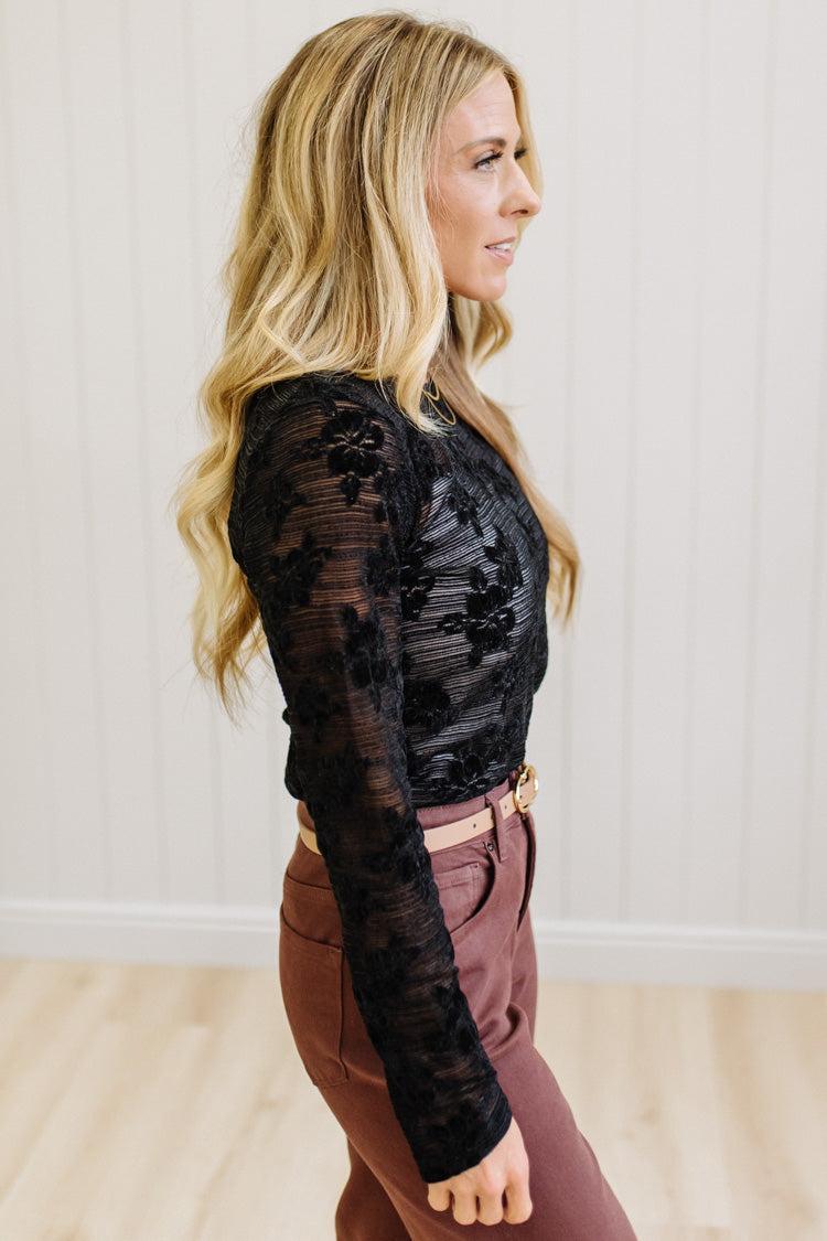 Blonde Woman Wearing A Floral Embroidered Stretch Lace Long Sleeve Top with Dark Jeans and Light Brown Belt.