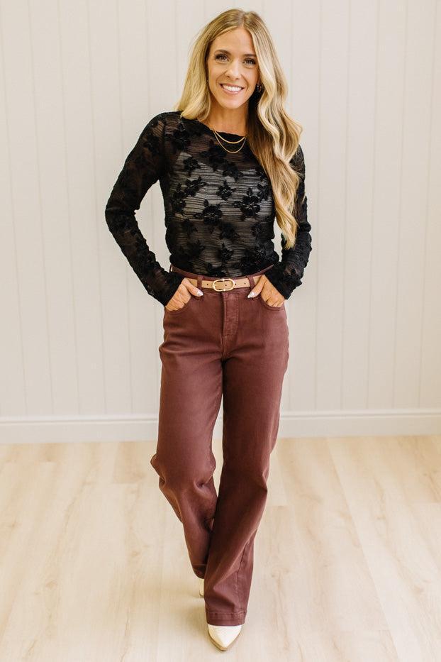 Blonde Woman Wearing A Floral Embroidered Stretch Lace Long Sleeve Top with Dark Jeans and Light Brown Belt.