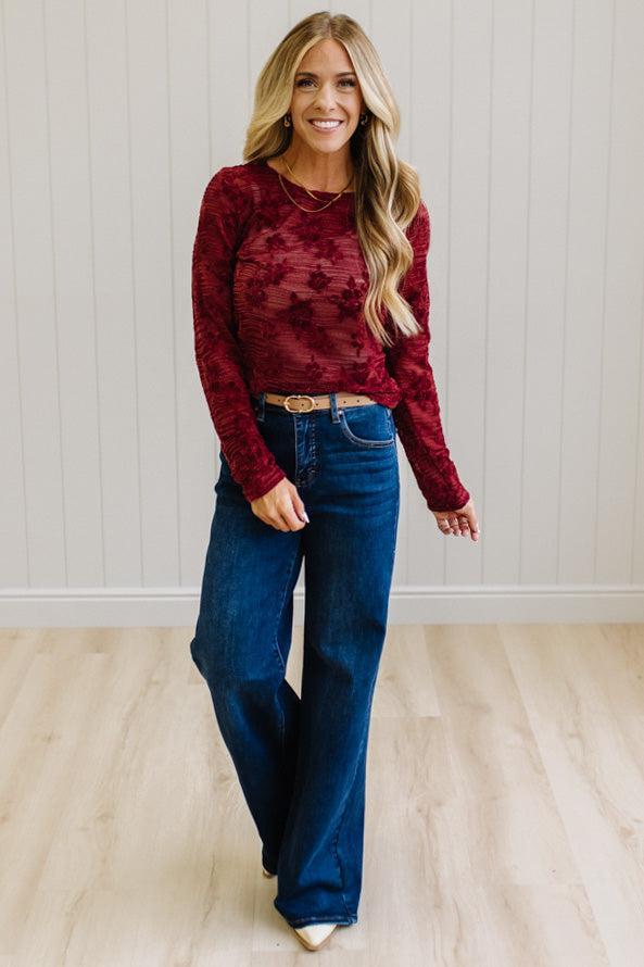 Blonde Woman Wearing A Floral Embroidered Stretch Lace Long Sleeve Top with Dark Jeans and Light Brown Belt.