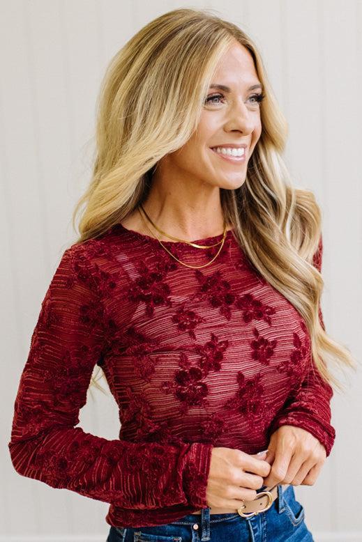 Blonde Woman Wearing A Floral Embroidered Stretch Lace Long Sleeve Top with Dark Jeans and Light Brown Belt.