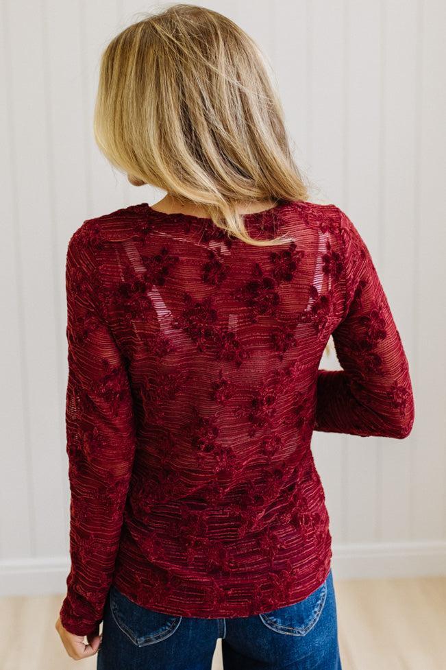 Blonde Woman Wearing A Floral Embroidered Stretch Lace Long Sleeve Top with Dark Jeans and Light Brown Belt.