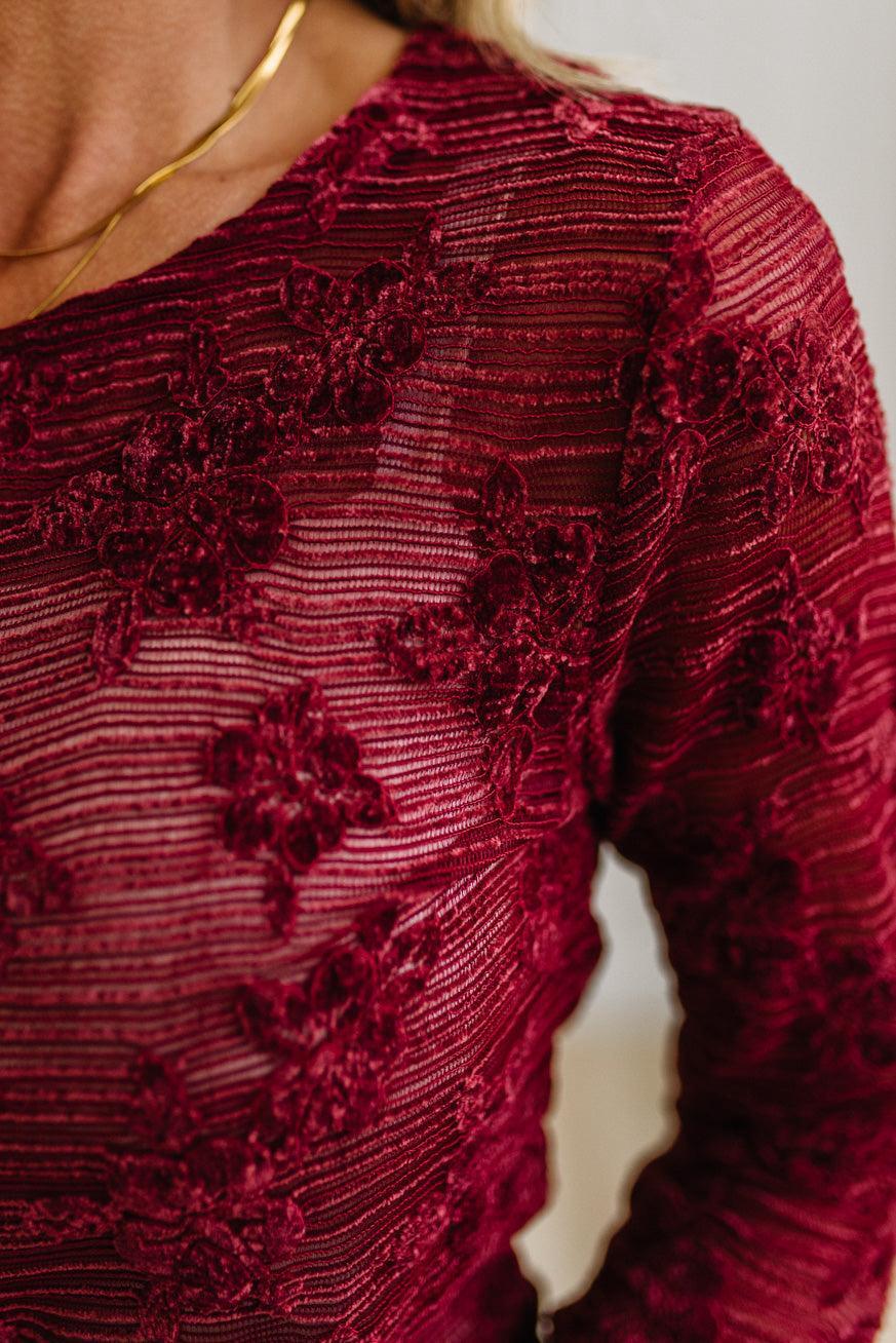 Blonde Woman Wearing A Floral Embroidered Stretch Lace Long Sleeve Top with Dark Jeans and Light Brown Belt.