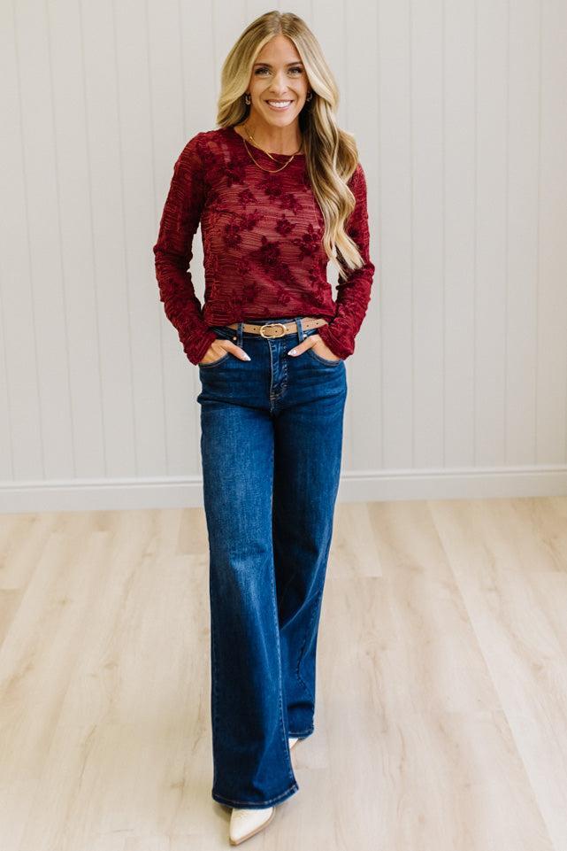 Blonde Woman Wearing A Floral Embroidered Stretch Lace Long Sleeve Top with Dark Jeans and Light Brown Belt.