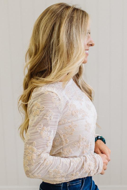 Blonde Woman Wearing A Floral Embroidered Stretch Lace Long Sleeve Top with Dark Jeans and Light Brown Belt.