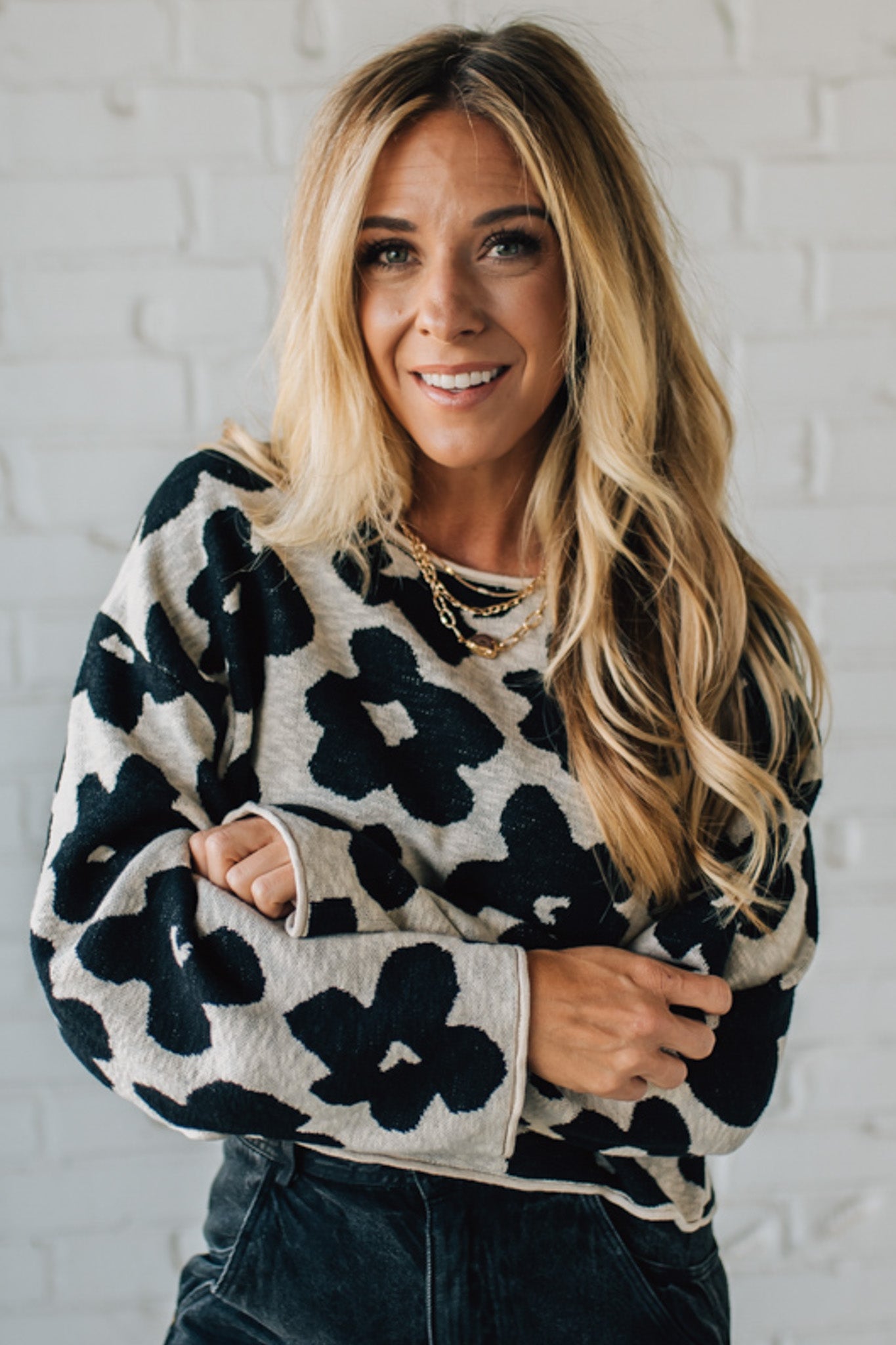 Woman wearing a black and white floral sweater against a white brick wall.