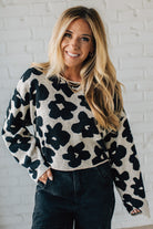 Woman wearing a black and white floral sweater against a white brick wall.