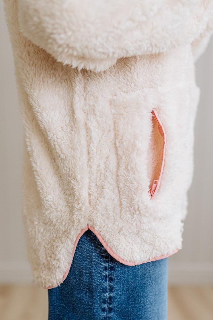 Close-up of a fluffy white garment with a pink trim worn over blue jeans.