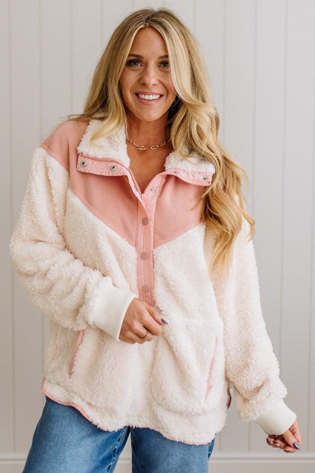 Woman wearing a pink and white sherpa jacket against a light background