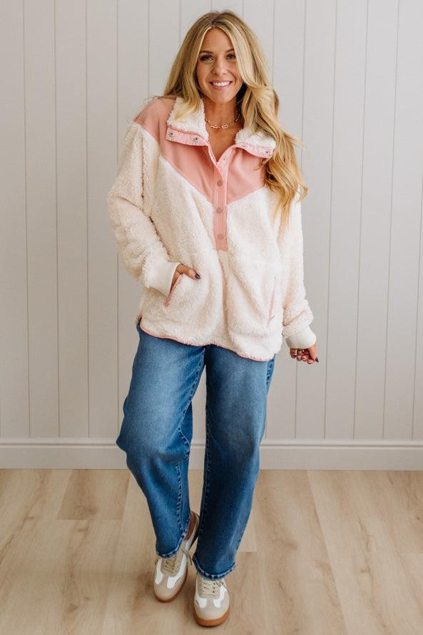 Woman wearing a white and pink fleece jacket with blue jeans indoors.
