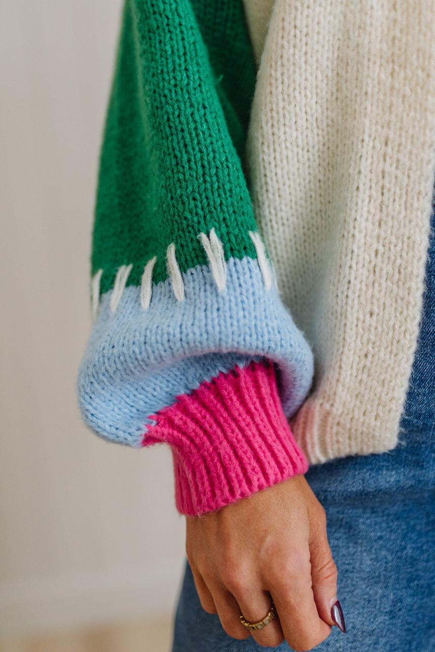 Close-up of a person wearing a colorful knit sweater with green, blue, pink, and beige sleeves.