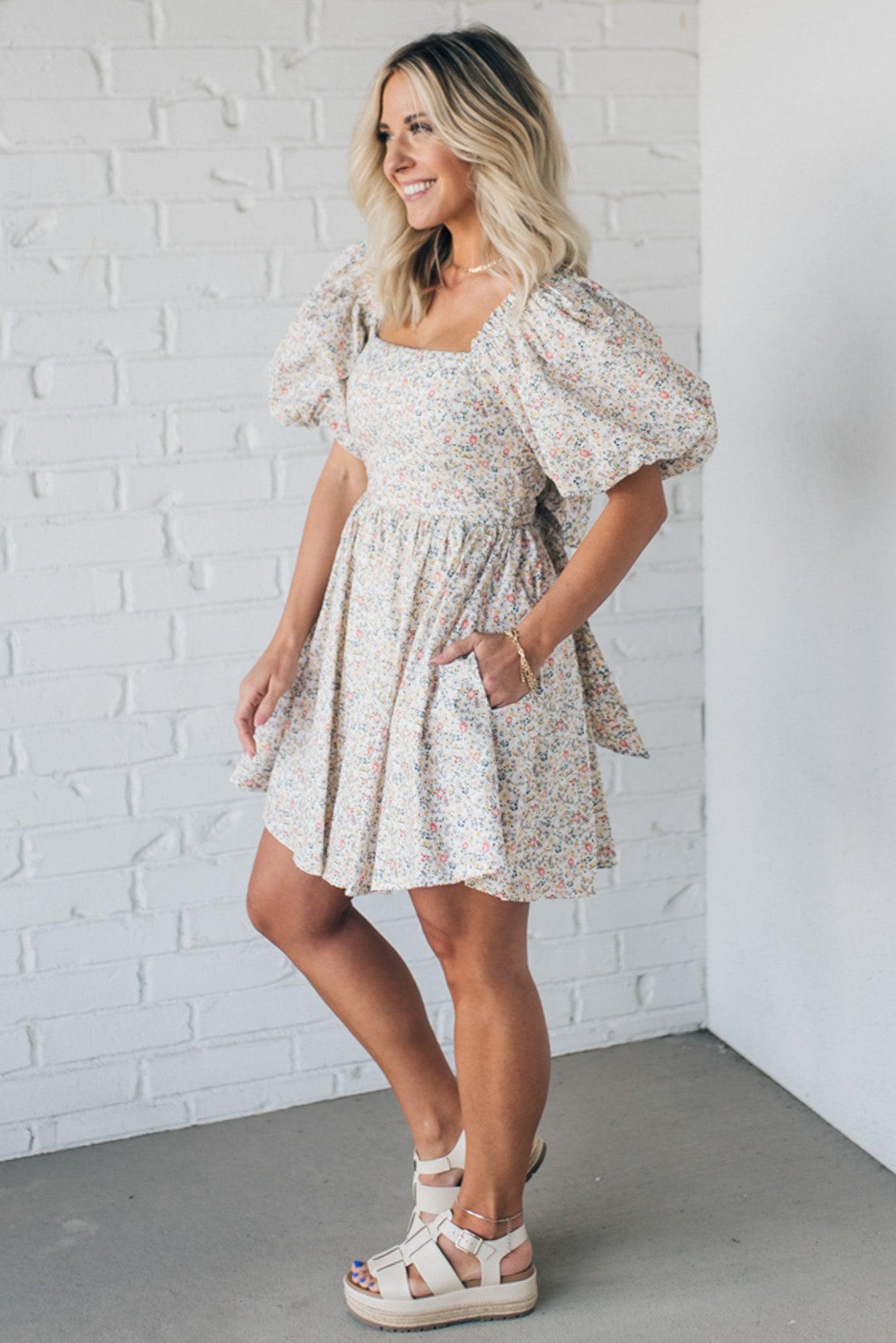 Blonde woman wearing a floral dress with puff sleeves and a large statement bow at the back.