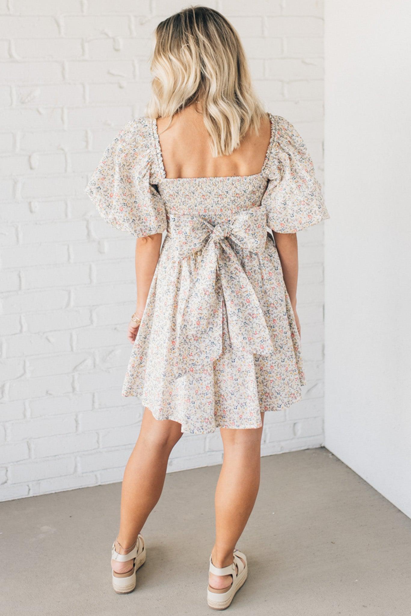 Blonde woman wearing a floral dress with puff sleeves and a large statement bow at the back.