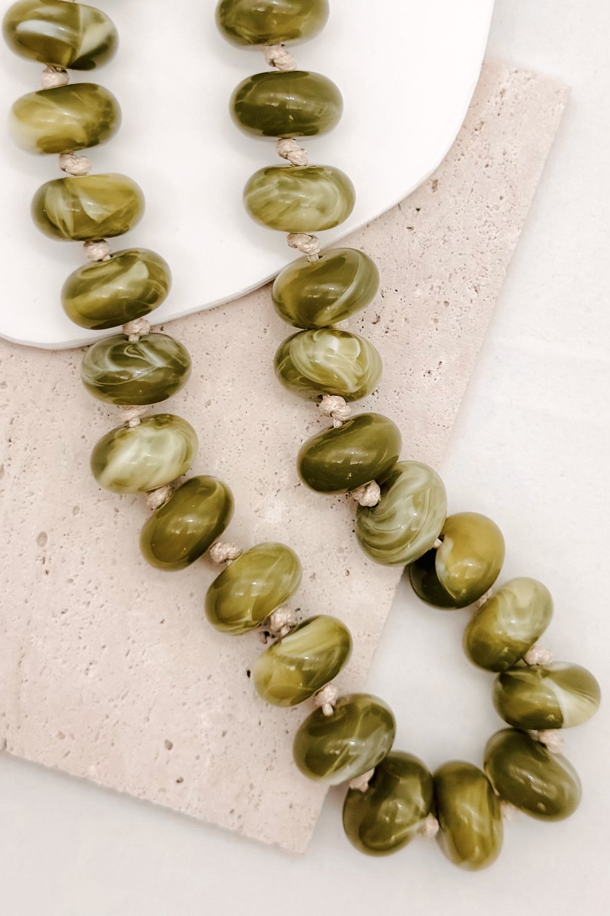 A CHUNKY BEADED NECKLACE WITH KNOTS BETWEEN EACH BEAD IN A GREEN MARBLED TONE.