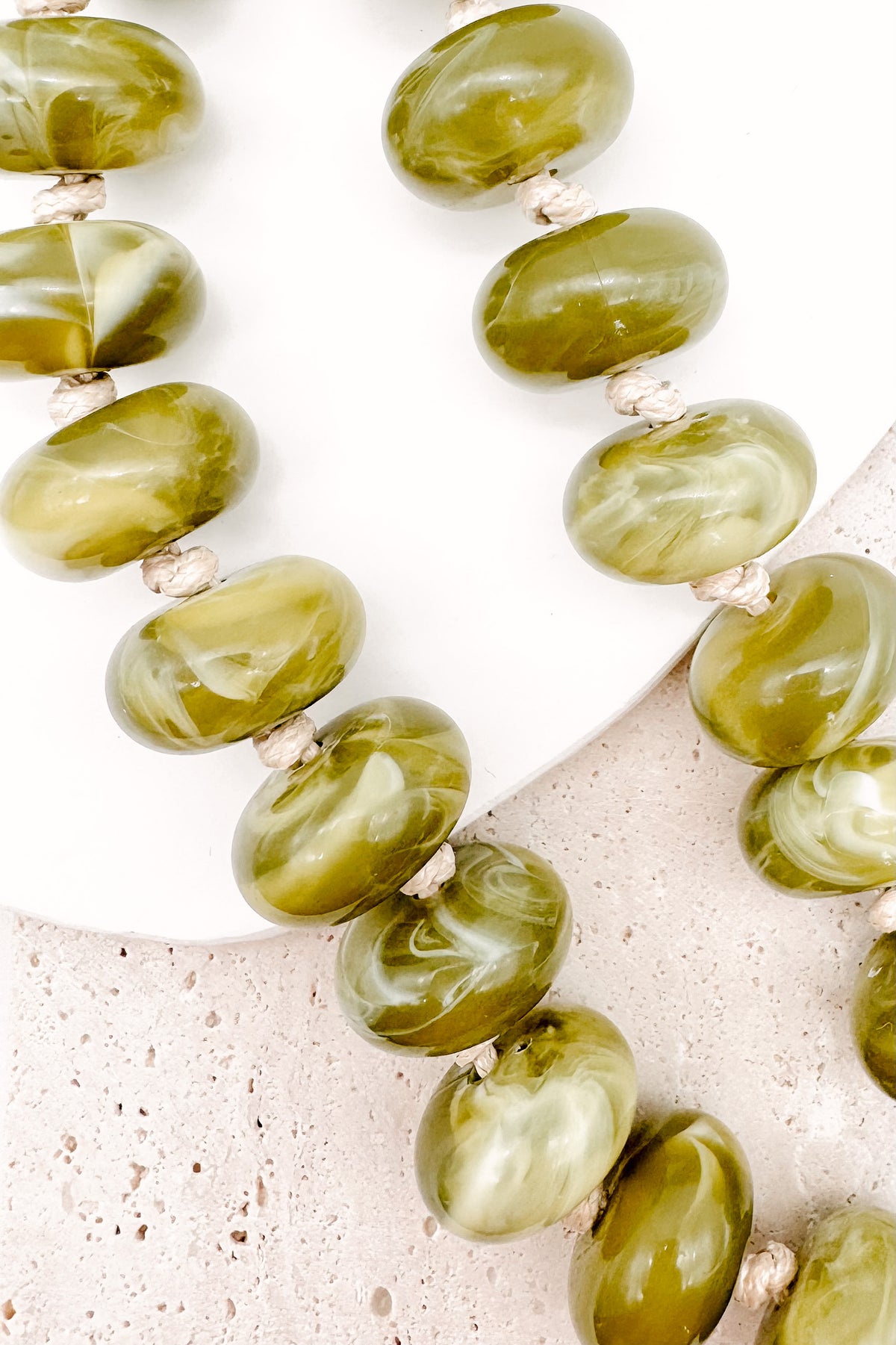 A CHUNKY BEADED NECKLACE WITH KNOTS BETWEEN EACH BEAD IN A GREEN MARBLED TONE.
