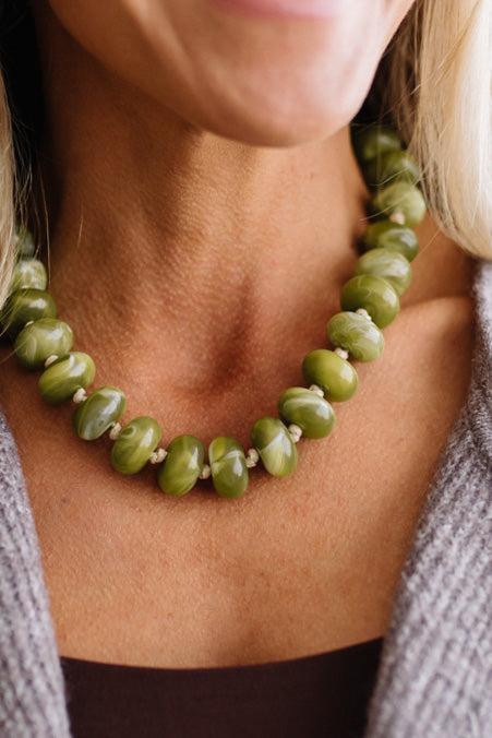 A CHUNKY BEADED NECKLACE WITH KNOTS BETWEEN EACH BEAD IN A GREEN MARBLED TONE.