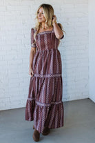 Woman wearing a patterned dress against a white brick wall.
