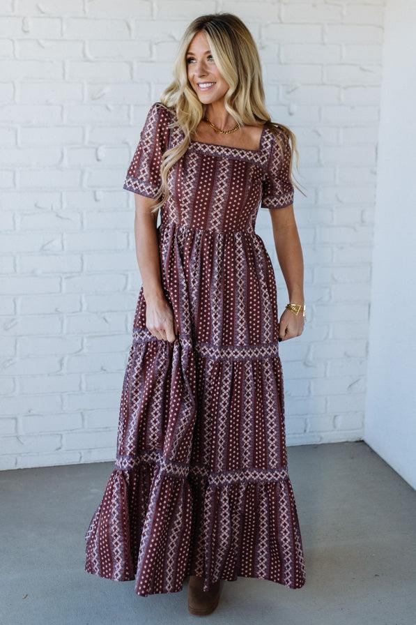 Woman wearing a patterned dress against a white brick wall.
