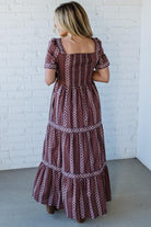 Woman wearing a patterned dress against a white brick wall.