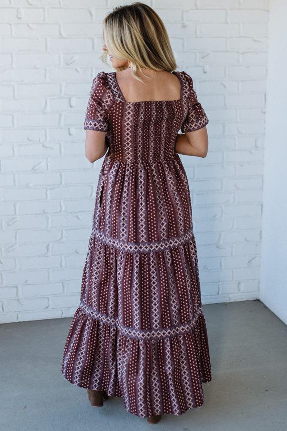 Woman wearing a patterned dress against a white brick wall.