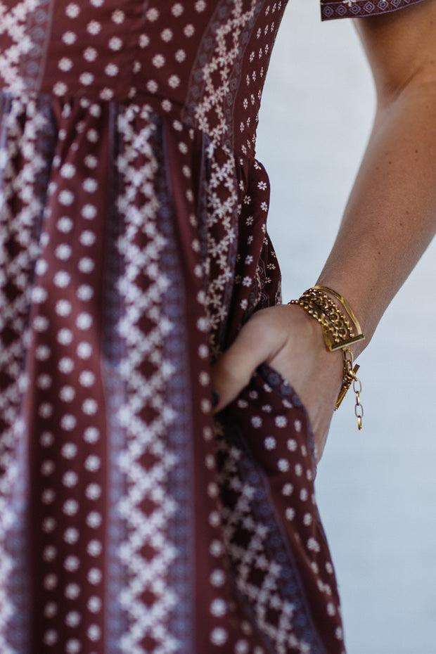Close-up of a person wearing a patterned dress with a gold bracelet on a blurred background