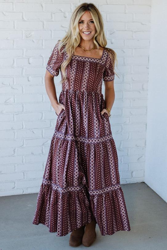 Woman wearing a patterned dress standing against a white brick wall.