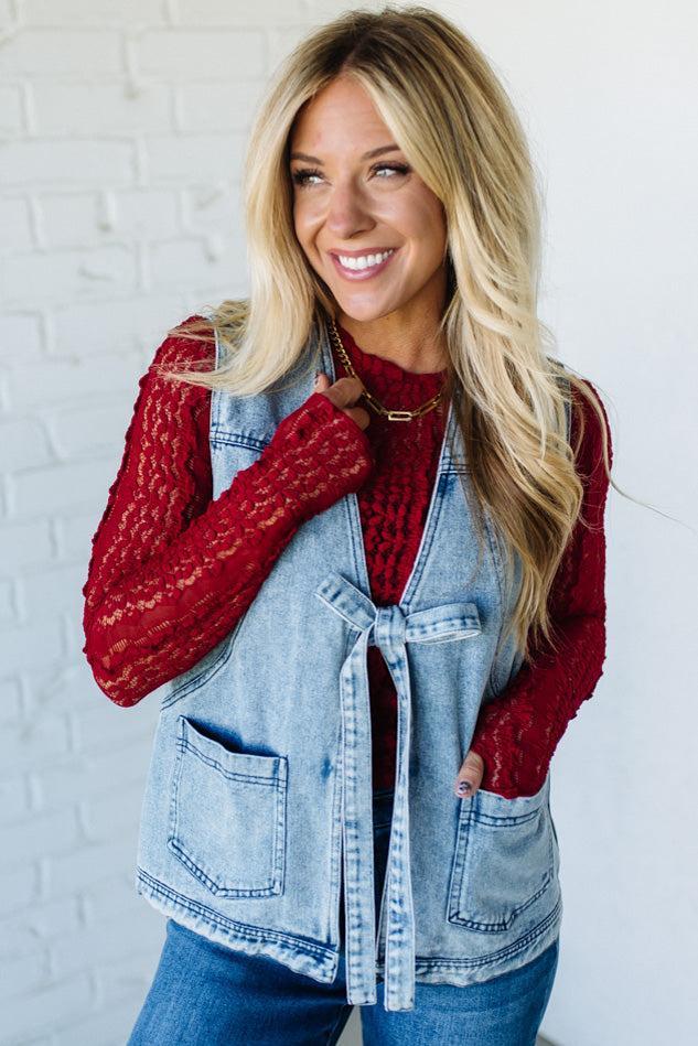 Woman wearing a denim vest over a red sweater with a white brick wall background
