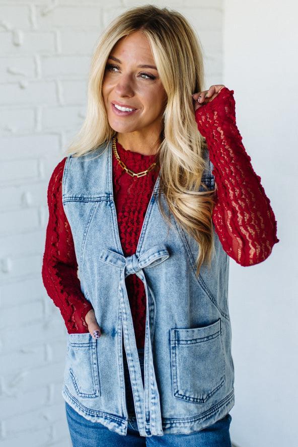 Woman wearing a denim vest over a red sweater with a white brick wall background