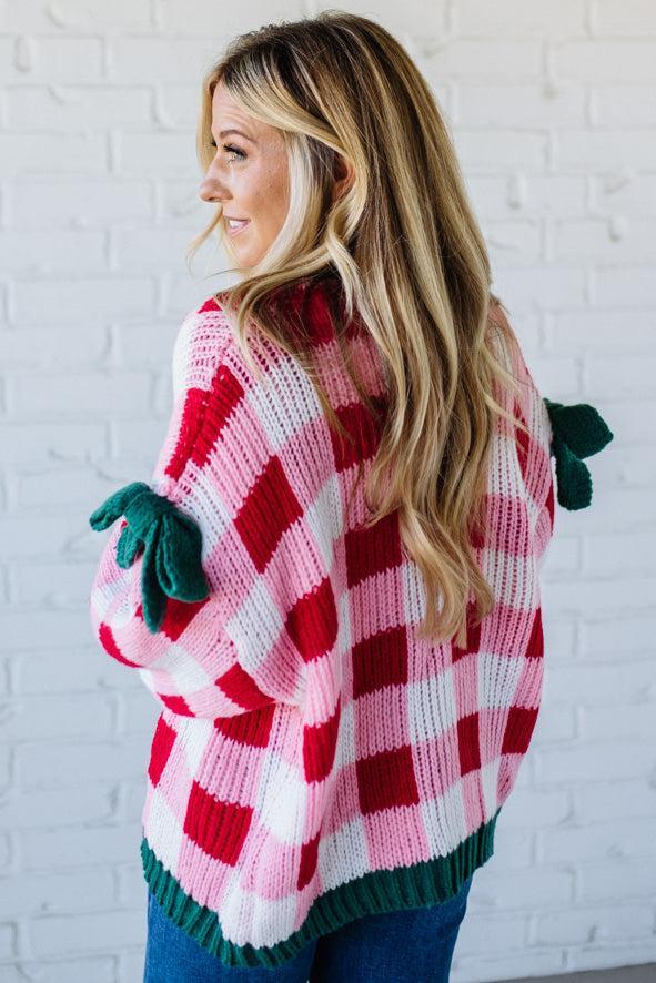 Person wearing a red and white checkered sweater with green accents against a white brick wall.