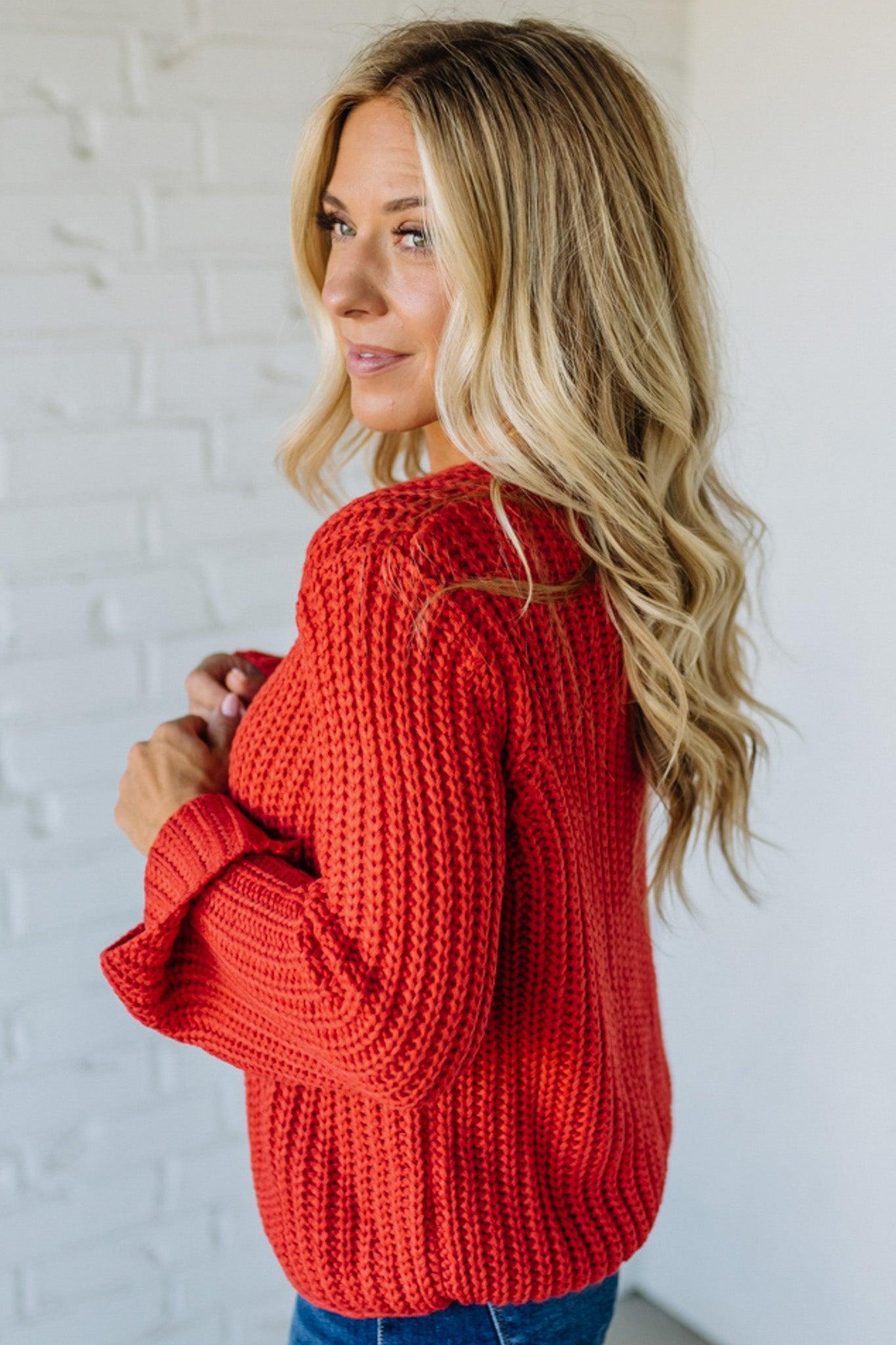 Woman wearing a red knitted sweater against a white brick wall.