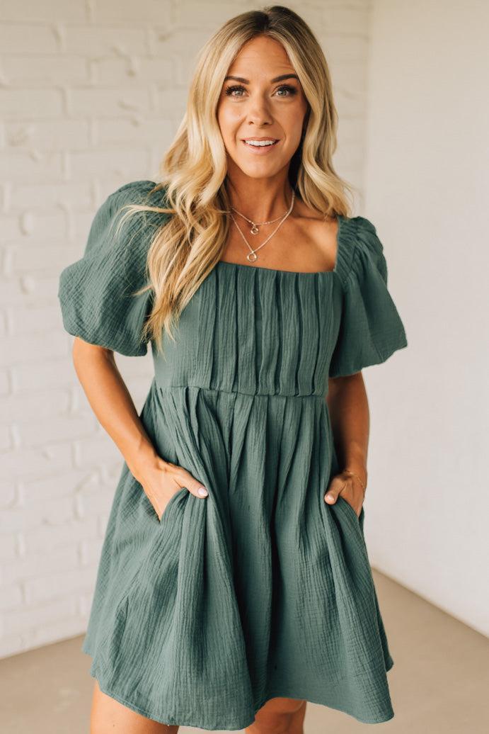Woman wearing a green dress against a white brick wall.