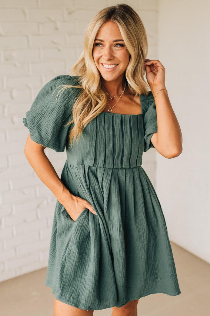 Woman wearing a green dress against a white brick wall.