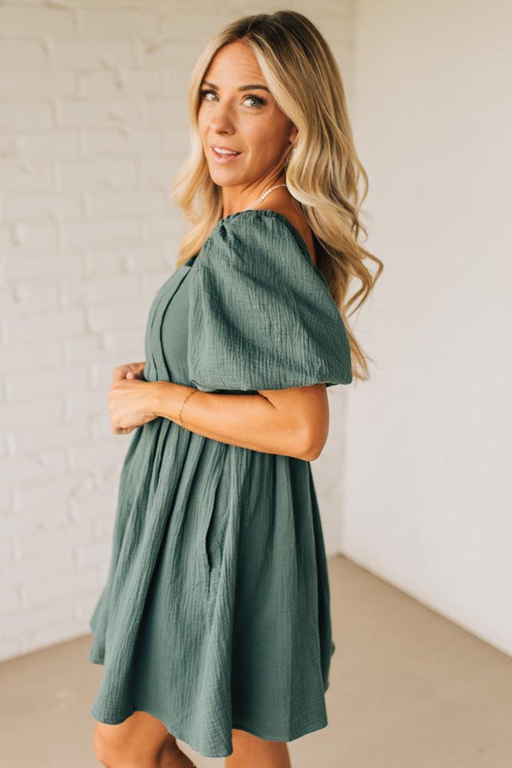 Woman wearing a green dress against a white brick wall.