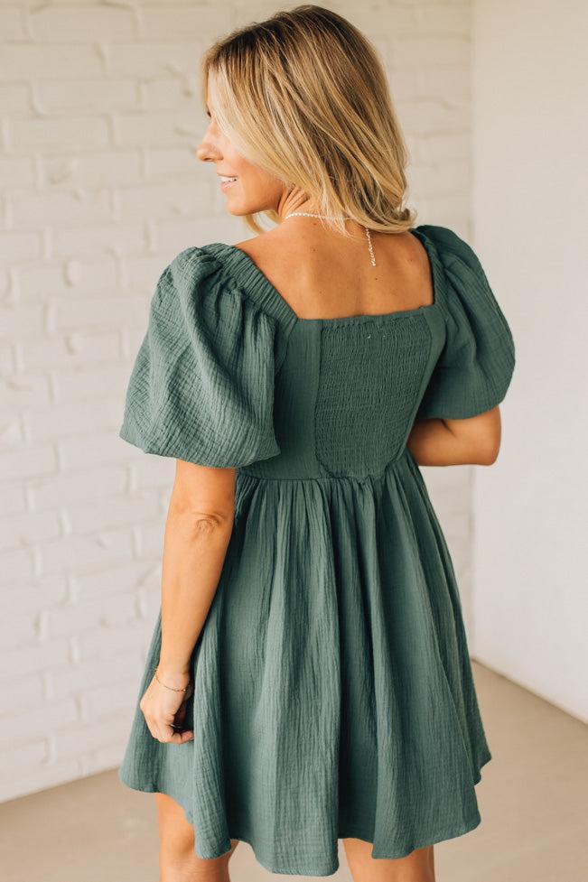 Woman wearing a green dress with puffed sleeves against a white brick wall.