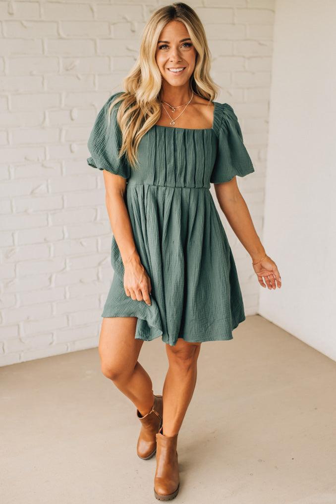 Woman wearing a green dress standing against a white brick wall.