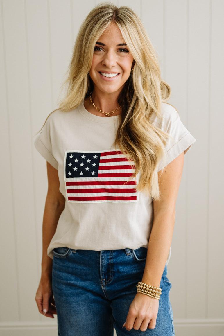 Woman wearing a white t-shirt with an American flag design and blue jeans.