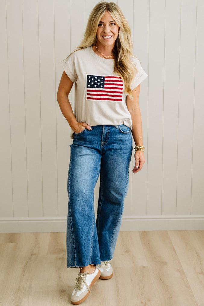 Woman wearing a t-shirt with an American flag design and blue jeans indoors.