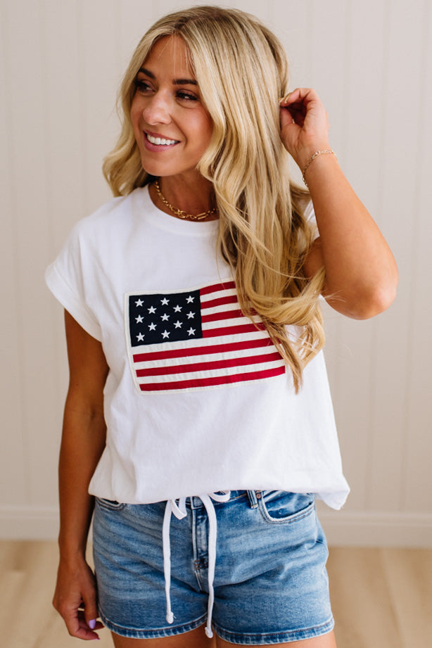 Woman wearing a white t-shirt with an American flag design and denim shorts.