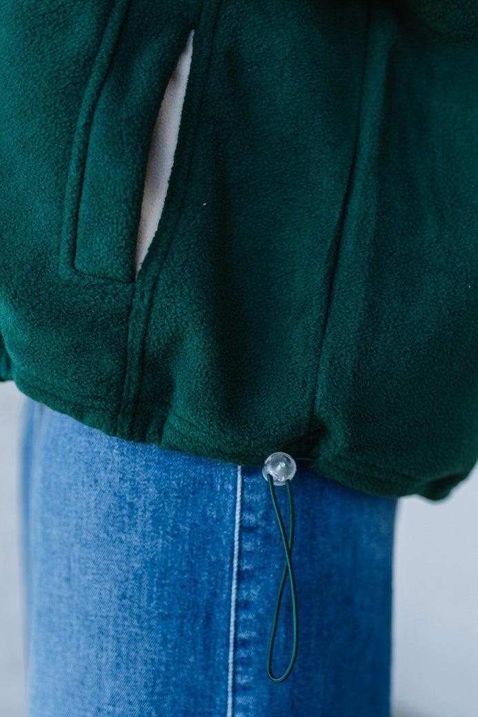 Green jacket with a close-up of a button on a blue denim skirt against a neutral background