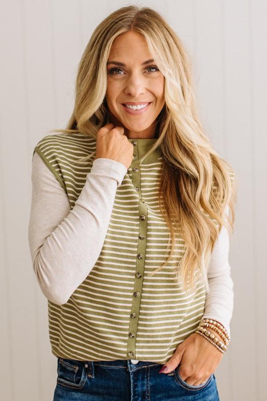 BLONDE WOMAN WEARING A MOCK NECK, FRONT BUTTON DETAILED, WITH CAP SLEEVES AND STRIPES. STANDING IN A WELL LIT STUDIO.