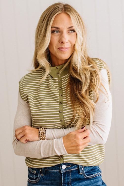 BLONDE WOMAN WEARING A MOCK NECK, FRONT BUTTON DETAILED, WITH CAP SLEEVES AND STRIPES. STANDING IN A WELL LIT STUDIO.