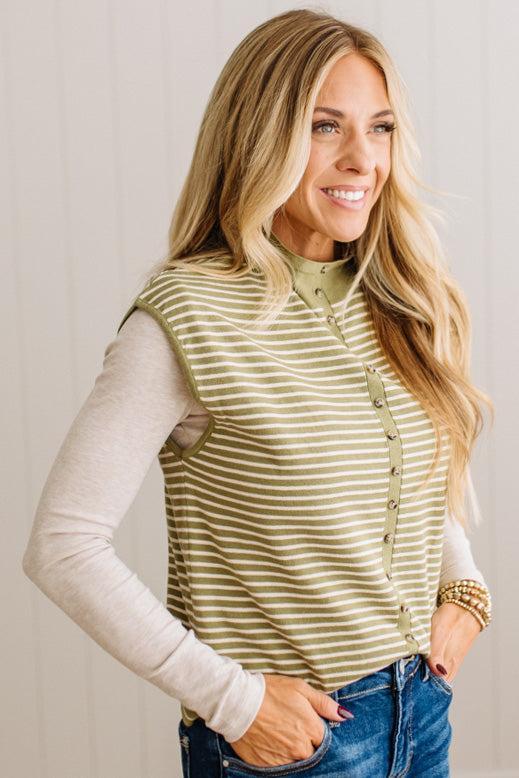 BLONDE WOMAN WEARING A MOCK NECK, FRONT BUTTON DETAILED, WITH CAP SLEEVES AND STRIPES. STANDING IN A WELL LIT STUDIO.