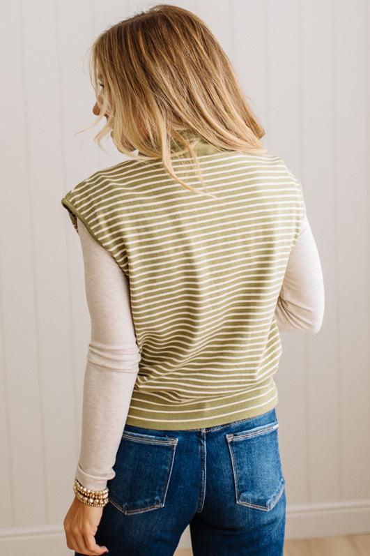 BLONDE WOMAN WEARING A MOCK NECK, FRONT BUTTON DETAILED, WITH CAP SLEEVES AND STRIPES. STANDING IN A WELL LIT STUDIO.