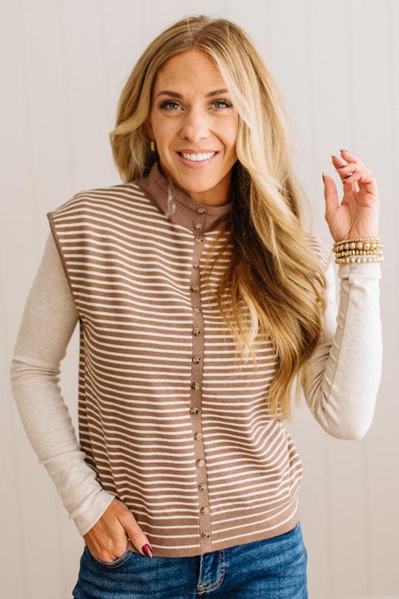 BLONDE WOMAN WEARING A MOCK NECK, FRONT BUTTON DETAILED, WITH CAP SLEEVES AND STRIPES. STANDING IN A WELL LIT STUDIO.