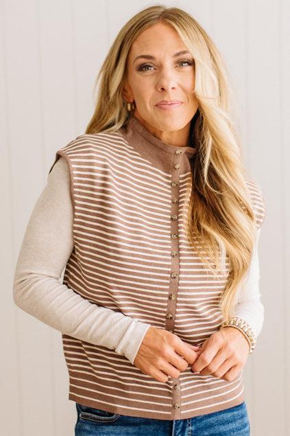 BLONDE WOMAN WEARING A MOCK NECK, FRONT BUTTON DETAILED, WITH CAP SLEEVES AND STRIPES. STANDING IN A WELL LIT STUDIO.