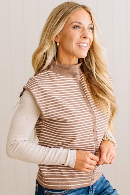 BLONDE WOMAN WEARING A MOCK NECK, FRONT BUTTON DETAILED, WITH CAP SLEEVES AND STRIPES. STANDING IN A WELL LIT STUDIO.